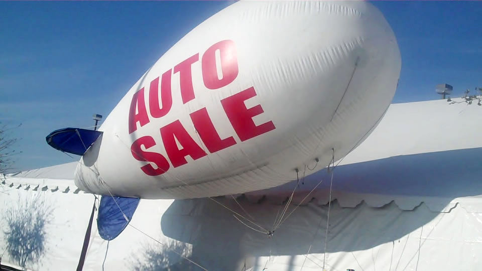 image of a large white and blue blimp that says auto sale on the side in red