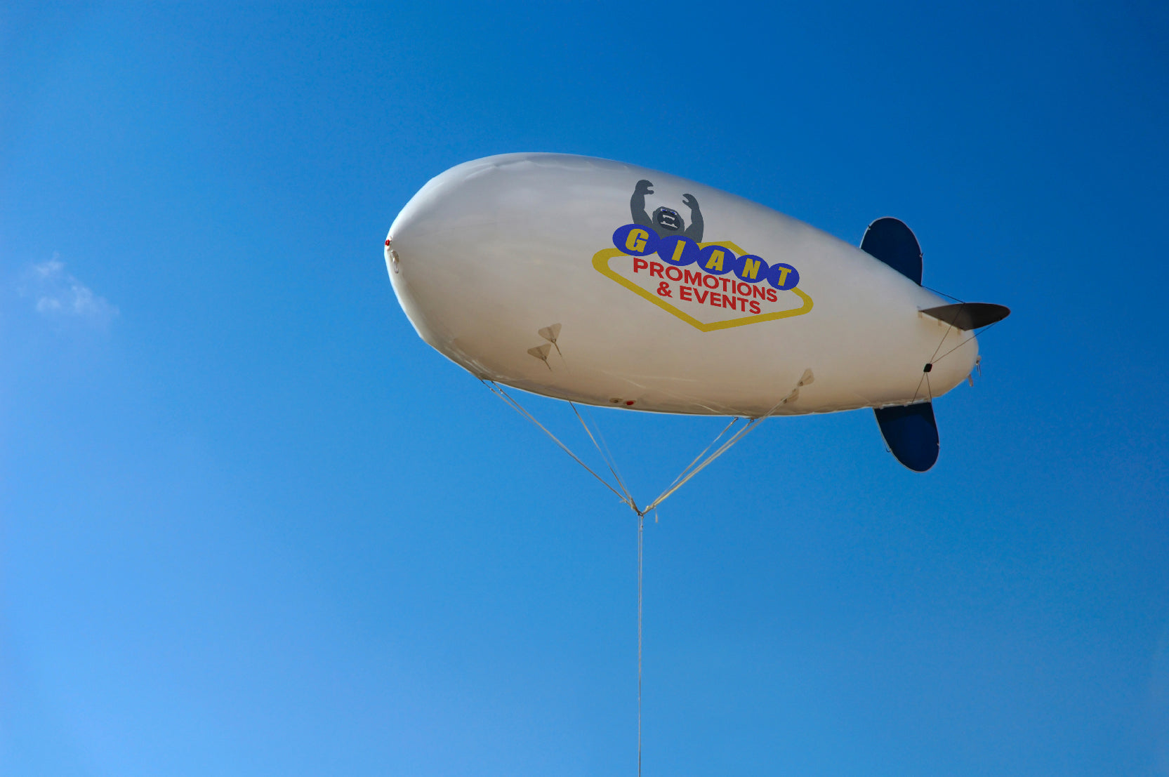 Image of a large white and blue blimp in the sky with Giant Promotions logo